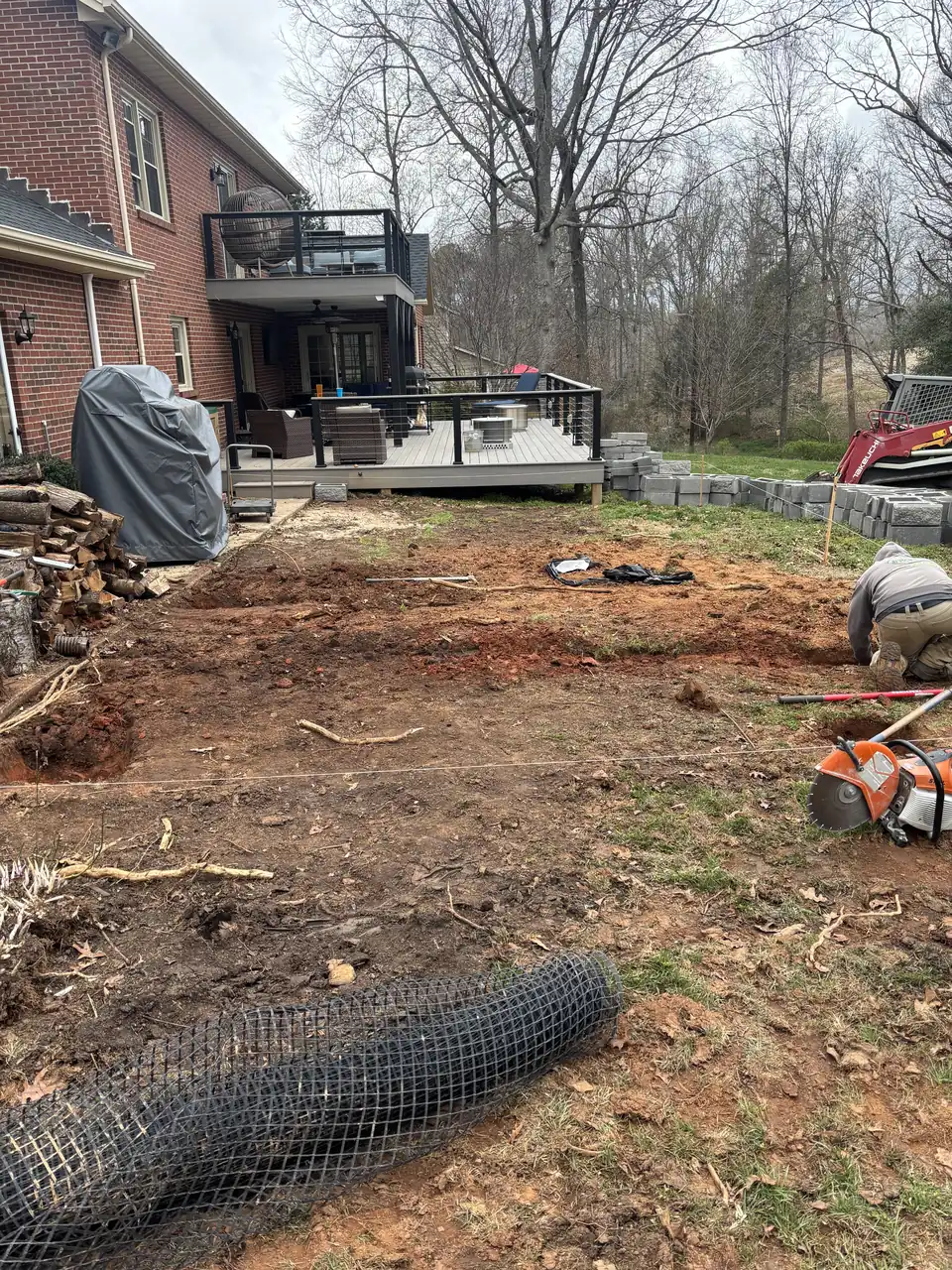 Area dug down to red clay, with a crew member working at the far edge