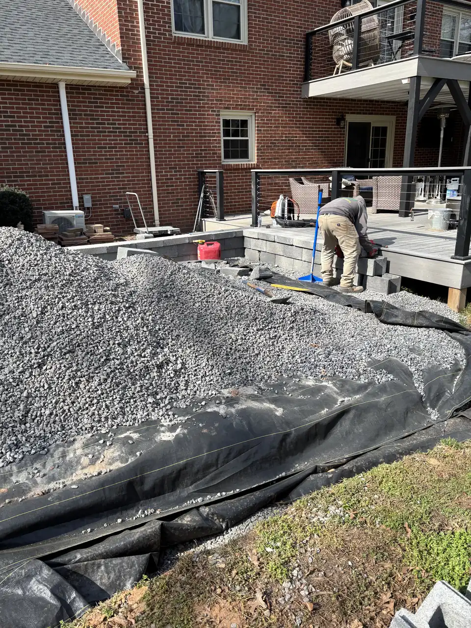 Crew member setting wall block along the edge of the compacted gravel base