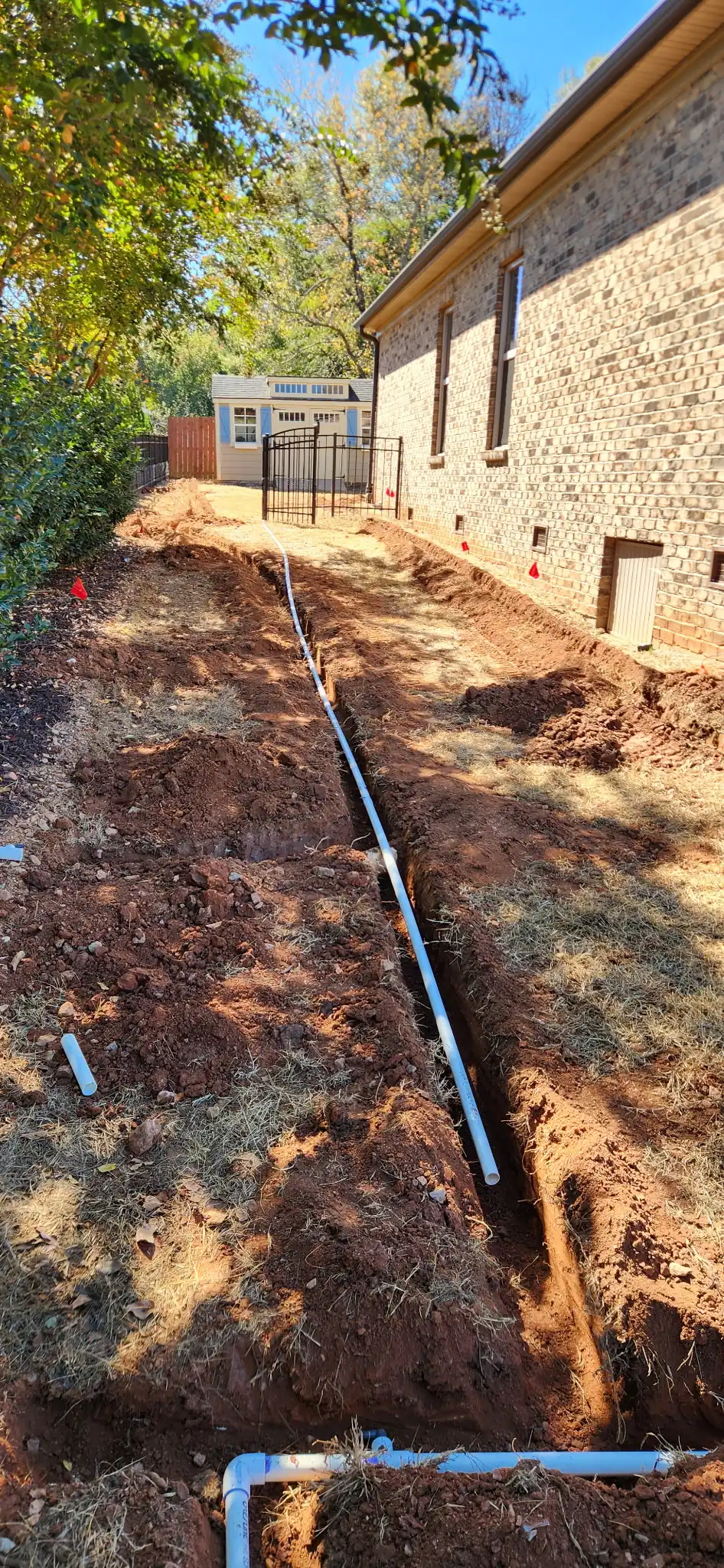 Trench dug along a brick foundation with white pipe laid in it
