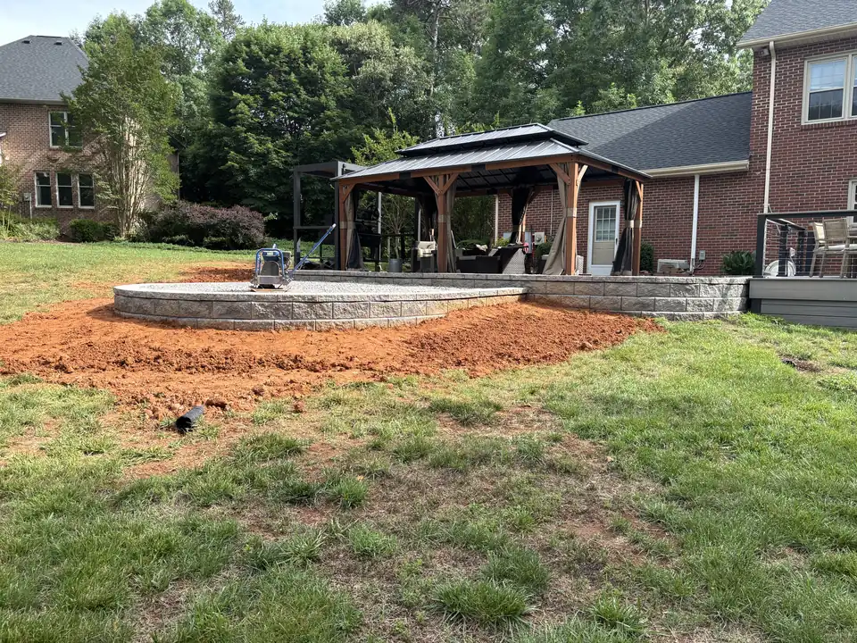 New block retaining wall holding a raised gravel pad, with freshly graded red clay around it
