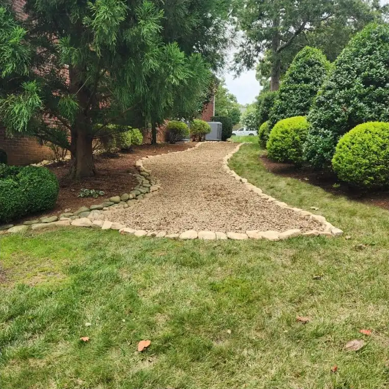 Curved gravel walkway edged with river rock between evergreens