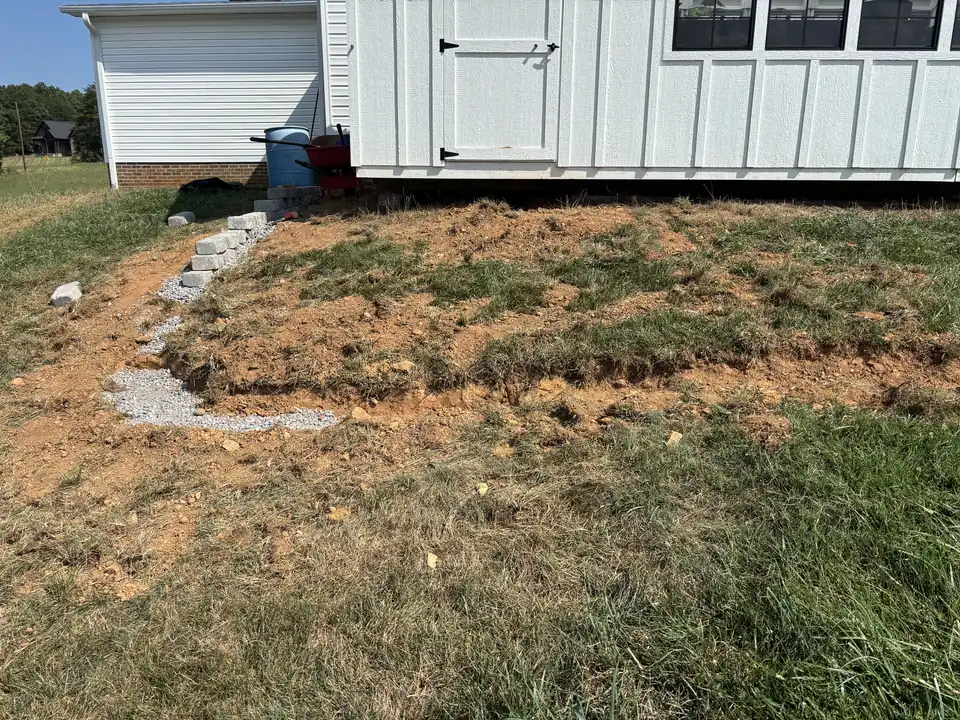 Sod cut back from a greenhouse, with a curved block edge started in the red clay