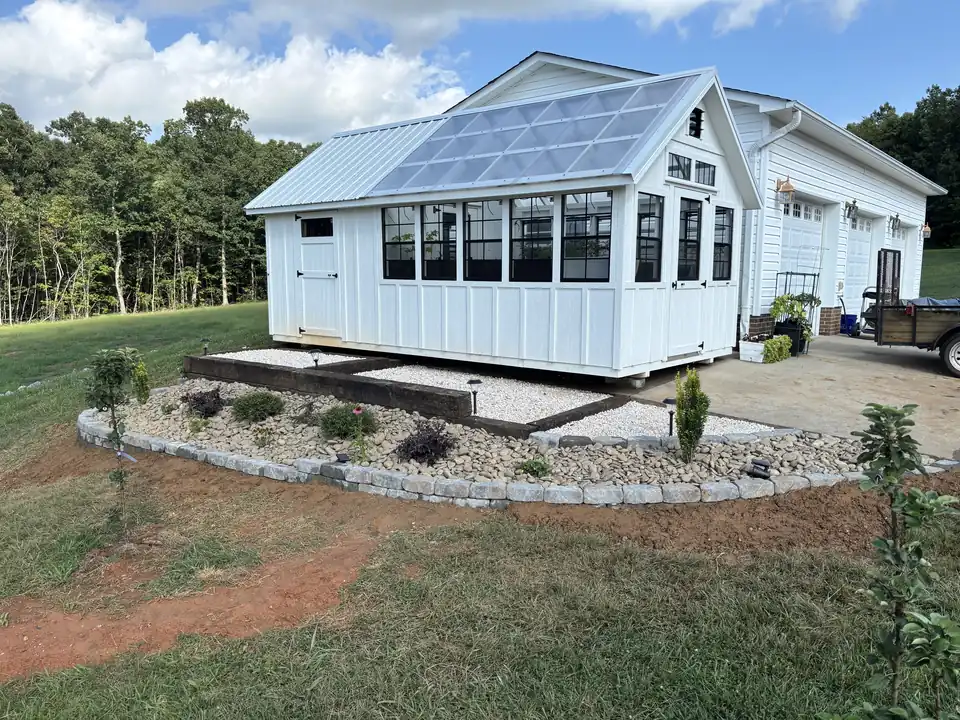 Finished river rock bed with block edging, shrubs and timber steps along a white greenhouse