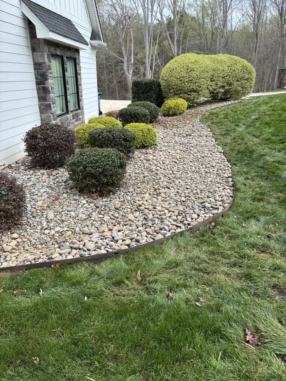 River rock bed with rounded shrubs curving along a stone-faced house