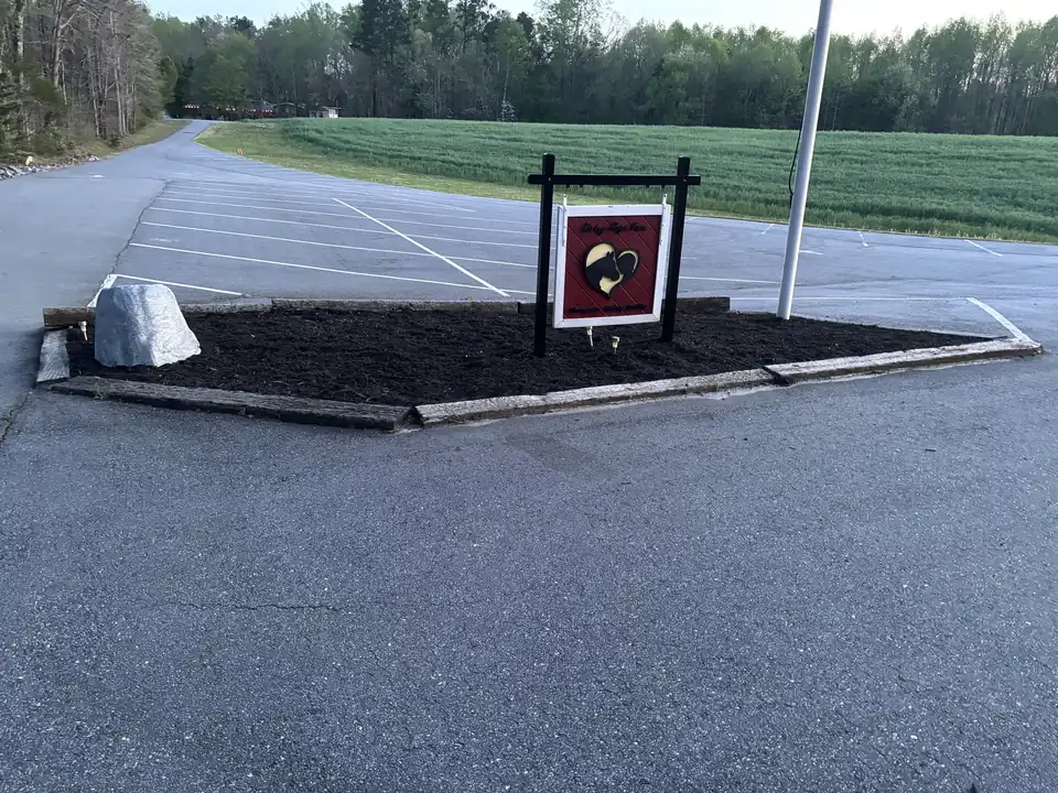 Fresh mulch bed around a business sign at the edge of a parking lot