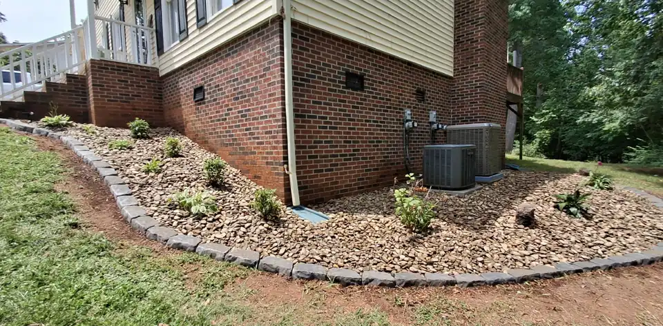 After: Bare ground along a brick foundation turned into a stone-edged rock bed