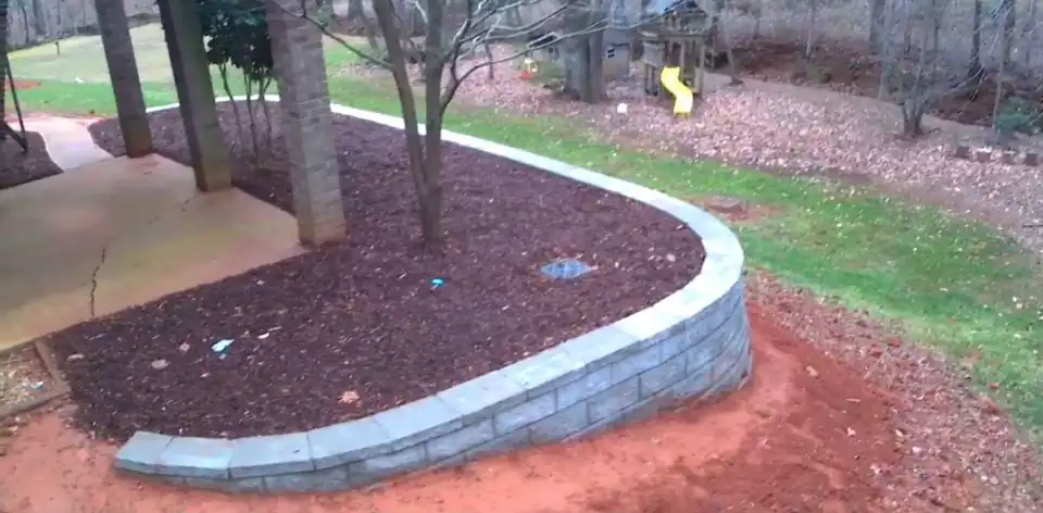Curved block retaining wall around a mulched bed under mature trees